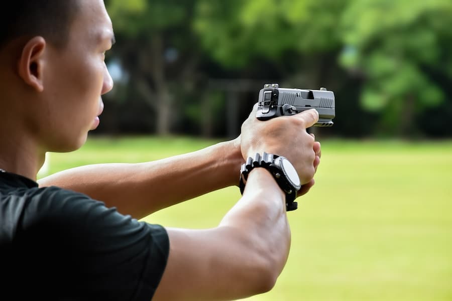 Asian young teens holding automatic black pistol in hands and ready to shoo
