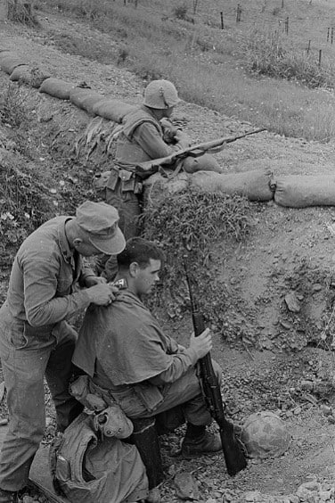 Three soldiers in a trench at Guantanamo Bay. Two are wielding M14 rifles, and one is giving a soldier a haircut