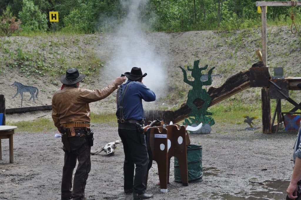 A CAS shooter engages a target with his lever-action rifle. To the left, the range officer with a timer that measures the shooter's stage time.