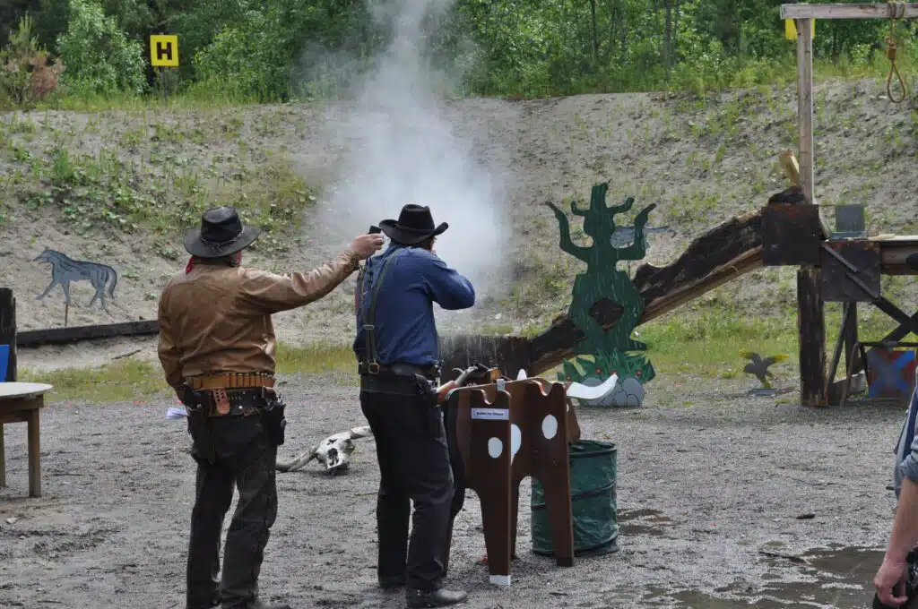 A CAS shooter engages a target with his lever-action rifle. To the left, the range officer with a timer that measures the shooter's stage time.